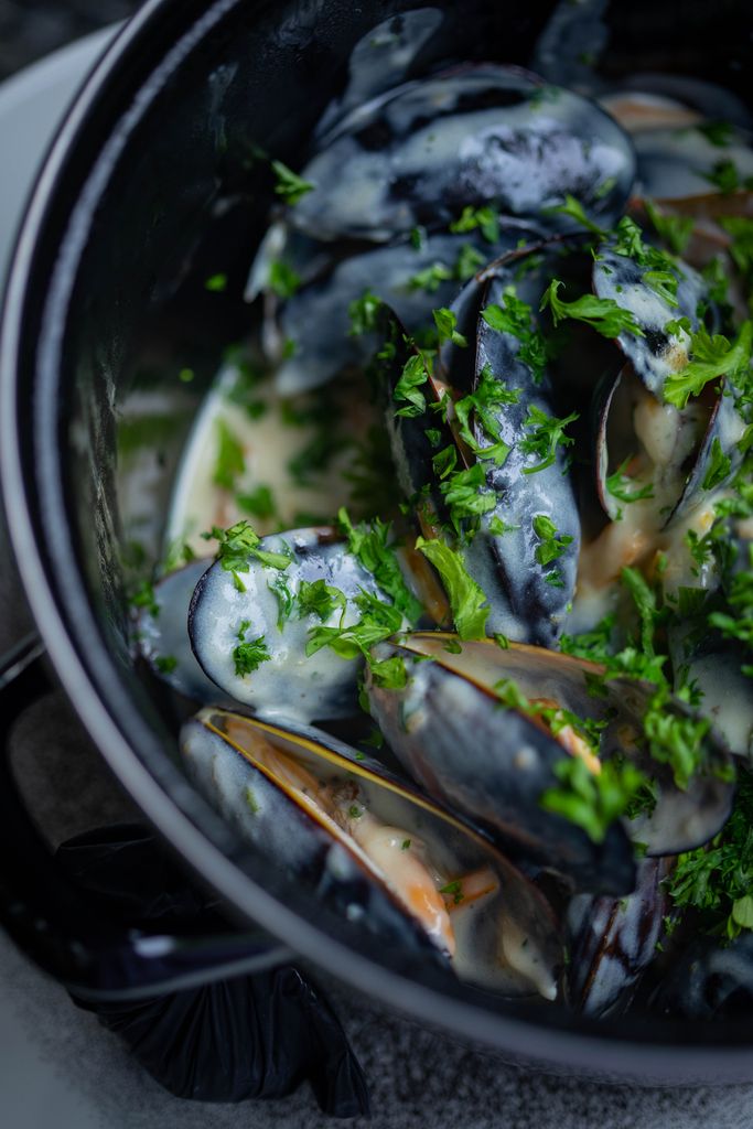 Freshly cooked mussels with creamy garlic sauce garnished with herbs in a black pot.